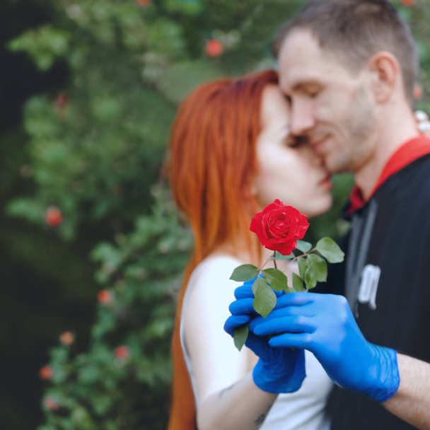 Unscharfes Bild eines jungen Paares mit einer Rose in der Hand. Das Konzept einer romantischen Beziehung mit Quarantäne, Safe Sex oder Schutzmaßnahmen. - Foto, Bild