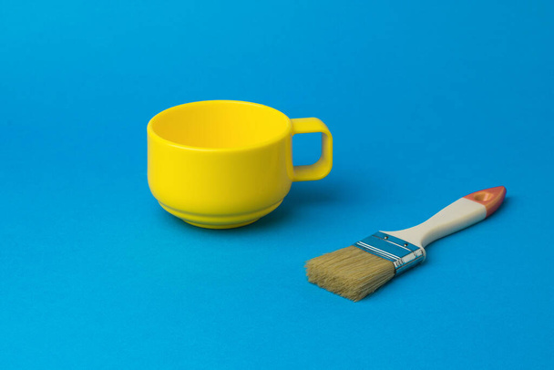 Pinsel und eine gelbe Tasse auf blauem Hintergrund. Der Farbtrend. - Foto, Bild