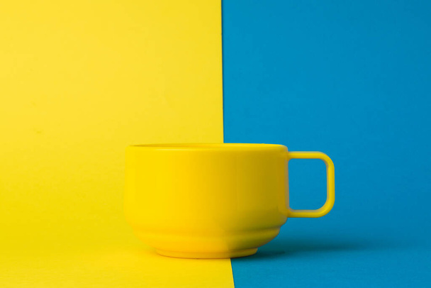Taza amarilla sobre fondo amarillo y azul. La tendencia del color. - Foto, Imagen