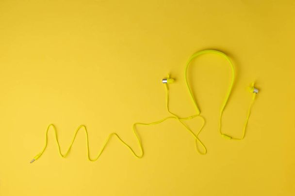Fones de ouvido esportivos amarelos com um fio em um fundo amarelo. Equipamento de reprodução de áudio móvel. - Foto, Imagem