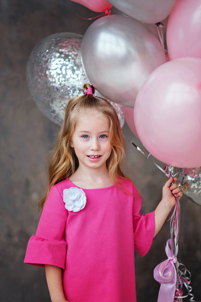 Portrait of Little Girl in pink dress with pink, grey balloons on grey background. Beautiful happy girl. The Concept Of Valentine's Day - Fotografie, Obrázek