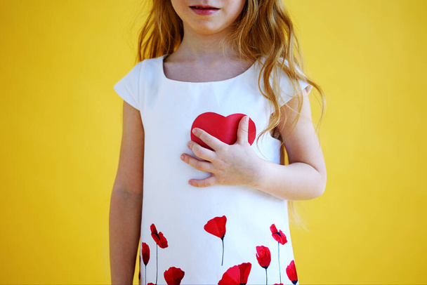 Küçük kız göğsüne kırmızı kağıt bir kalp bastırıyor. Sağlık ve Sevgililer Günü konsepti - Fotoğraf, Görsel