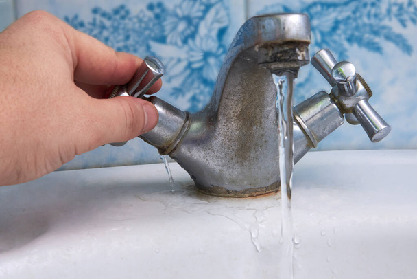 Вода течет из ржавого старого крана в ванной комнате, водопровод. - Фото, изображение