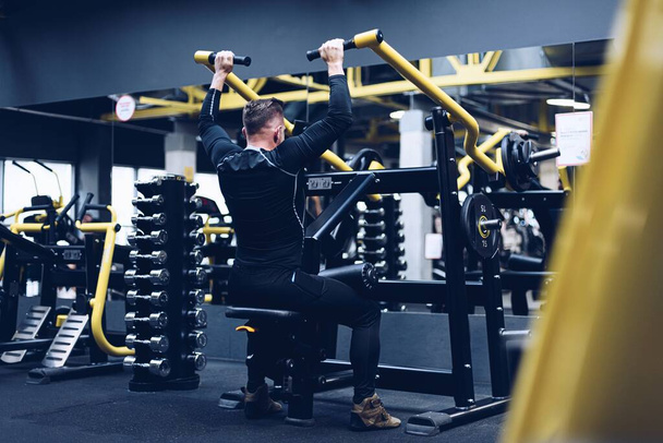 Ein gesunder, fitter Bodybuilder trainiert mit Geräten im Fitnessstudio den oberen Teil seiner Muskeln. - Foto, Bild