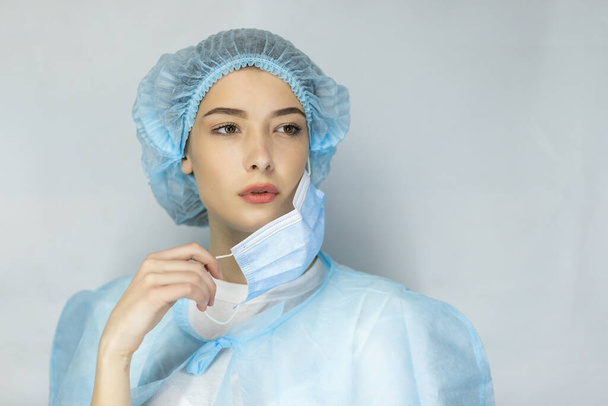 Portrait of tired young doctor taking off medical face mask isolated over gray background - Valokuva, kuva