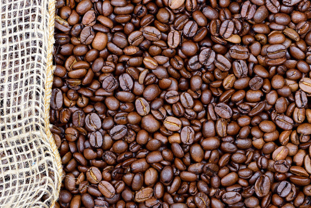 Background, close-up and texture of roasted coffee beans with a piece of jute running along the edge - Photo, Image