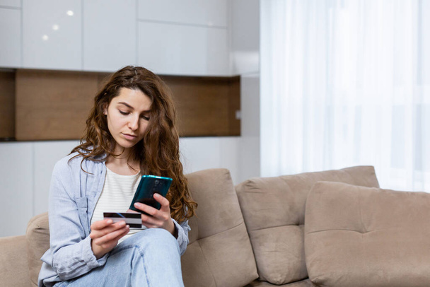 Portrait happy female shopper using instant easy mobile payments making purchase in online store young woman customer holding credit card and smartphone sitting on couch at home - Fotografie, Obrázek