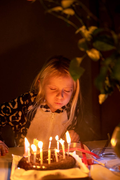 kleines Mädchen, das bei Geburtstagsparty im Schlafanzug mit geschlossenen Augen Kerzen auspustet, verschwommenes Gesicht, senkrecht - Foto, Bild