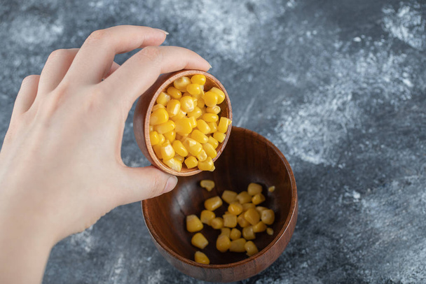 Añadir a mano semillas de palomitas de maíz en un tazón de madera - Foto, Imagen