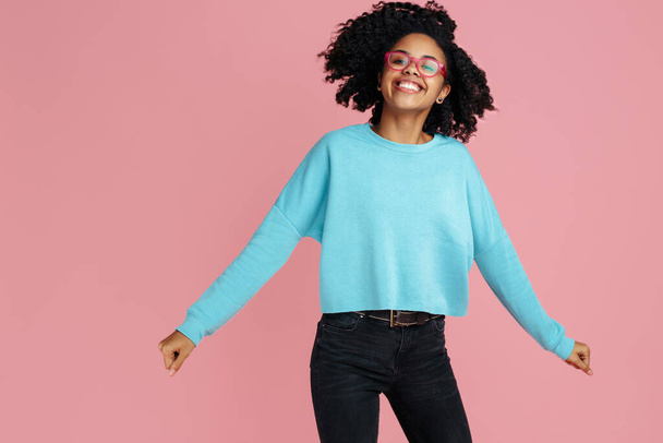 Excited african american young woman with bright smile dressed in casual clothes dance over pink background. - Fotografie, Obrázek