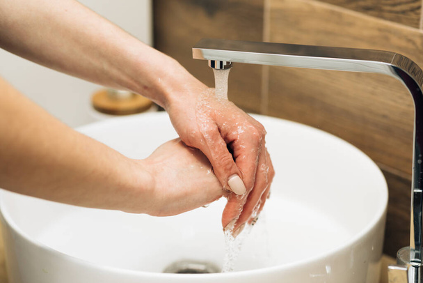 Concept of health, cleaning and preventing germs and coronavirus from contacting hands. Hands of woman wash their hands in a sink to wash the skin and water flows through the hands - Фото, изображение