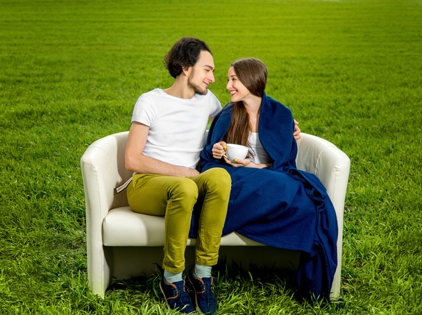 Νεαρό ερωτευμένο ζευγάρι κάθεται στον καναπέ στο πράσινο πεδίο - Φωτογραφία, εικόνα