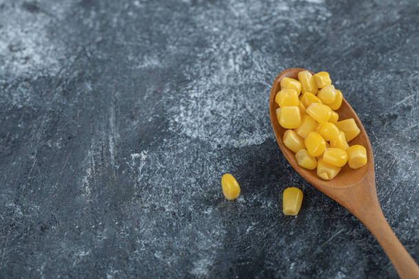 Ein Kochlöffel voller Popcorn-Samen auf einem Marmorgrund - Foto, Bild