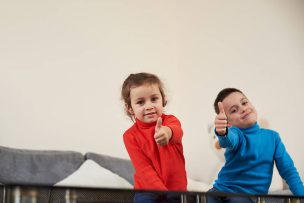 Дівчинка і хлопчик показують великі пальці вгору і посміхаються в камеру
 - Фото, зображення