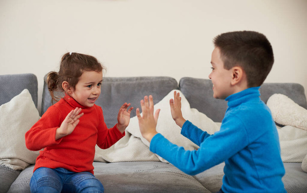 Brother and sister clap their hands sitting on the gray sofa - Photo, image
