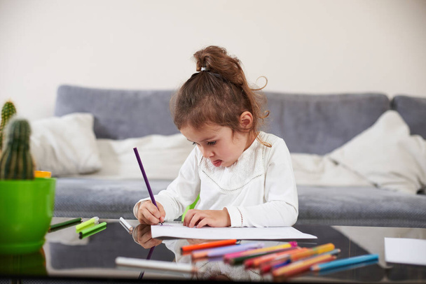 Ένα κορίτσι προσχολικής ηλικίας επικεντρωμένο στη ζωγραφική. Έννοια της προσχολικής εκπαίδευσης στο σπίτι. - Φωτογραφία, εικόνα