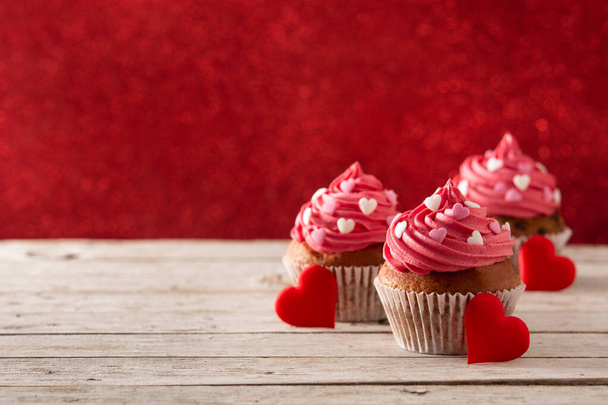 木製のテーブルと赤の背景にバレンタインデーのための砂糖の心で飾られたカップケーキ - 写真・画像