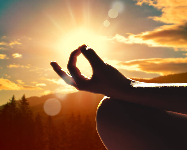 Close-up van een hand in een meditatie houding. Zonsondergang in de bergen. - Foto, afbeelding