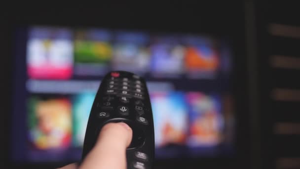 Man kijken Smart TV en met behulp van moderne zwarte afstandsbediening, wazig TV in de achtergrond. Close-upweergave - Video
