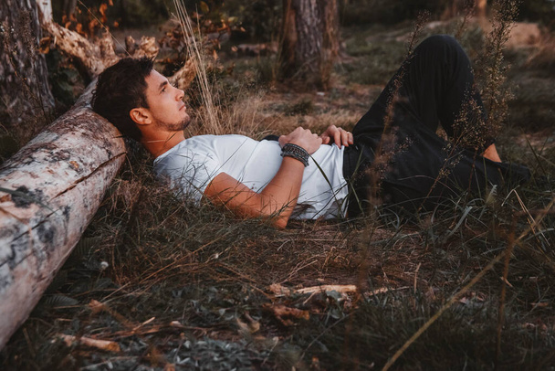 Чоловік лежить на траві, спираючись на колоду посеред лісу, відпочиває. Місце для тексту або реклами
. - Фото, зображення