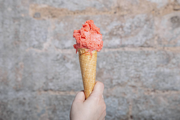 Mano sosteniendo el cono de helado artesanal sabor fresa. Helado de fresa servido en un cono de gofre. Helado italiano - Foto, imagen