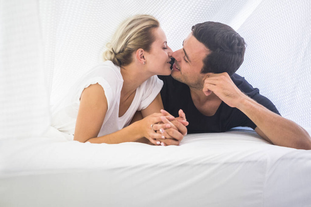 Love and valentine's day celebration at home in the bedroom with young beautiful couple kissing in the morning waking up - 写真・画像