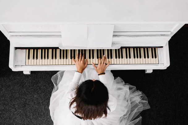 Hermosa mujer vestida con vestido blanco tocando el piano blanco. Vista superior. - Foto, imagen