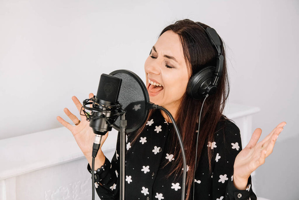 Retrato de mulher bonita em fones de ouvido canta uma música perto de um microfone em um estúdio de gravação.. Lugar para texto ou publicidade. - Foto, Imagem