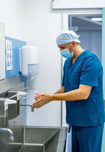 Surgeon in hospital washing thoroughly his hands before performing a surgery. Doctors washing hands before operation. - Фото, зображення