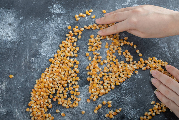 Hand verdelen van ongekookte popcorn zaden op een marmeren achtergrond - Foto, afbeelding