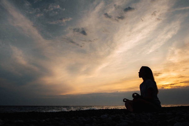 Silueta ženy v meditaci pózuje na mořské pláži během surrealistického západu slunce na mořském pozadí a dramatické obloze. Pojem uvolnění svobody. Místo pro text nebo reklamu. - Fotografie, Obrázek
