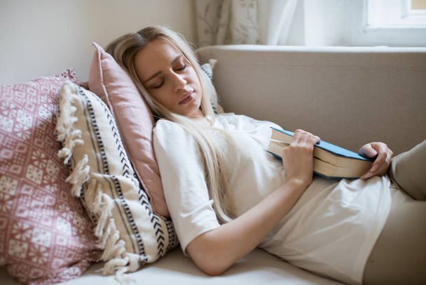 stanca femmina sentiva un sonno con il libro in mano sdraiata sul divano al chiuso.  - Foto, immagini