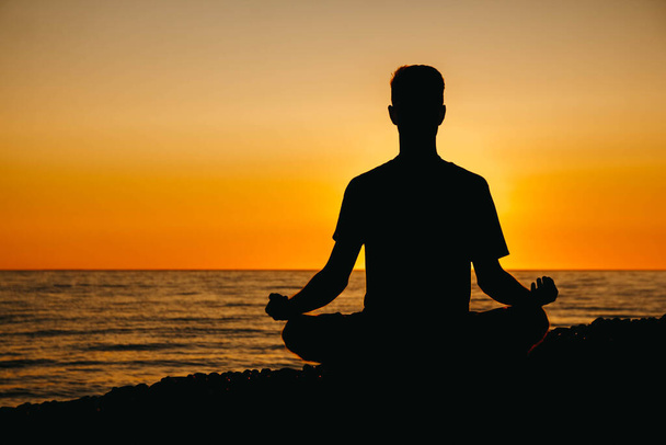 Silhouette d'un homme en méditation posant sur la plage sur fond marin et au coucher du soleil. Concept de liberté détente. Lieu de texte ou de publicité. - Photo, image