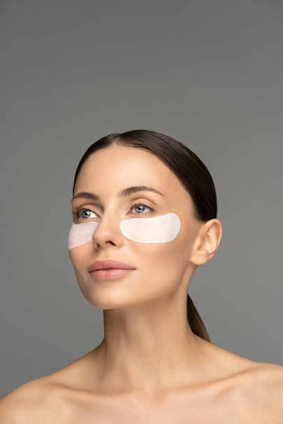 Woman applying hydrogel under-eye recovery patches enriched with collagen, vitamin E, provides intensive hydration and diminishes the signs of aging, helps reduse eye puffiness. Face skincare beauty. - Фото, изображение