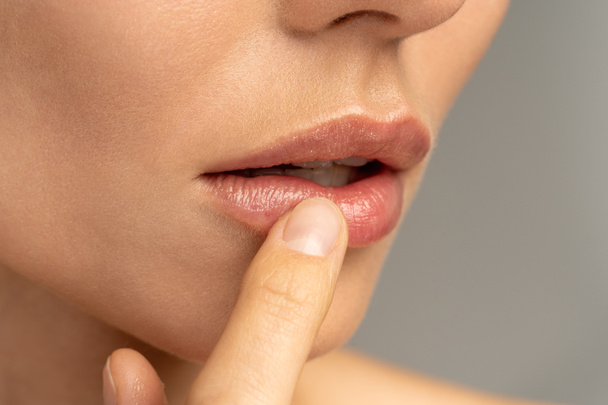 Zbliżenie kobiety stosującej balsam nawilżający na usta palcem, aby zapobiec suchości i pękaniu w zimnej porze roku. Ochrona ust. - Zdjęcie, obraz