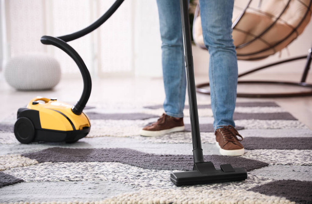 Young man cleaning carpet with vacuum cleaner at home, closeup - Fotó, kép