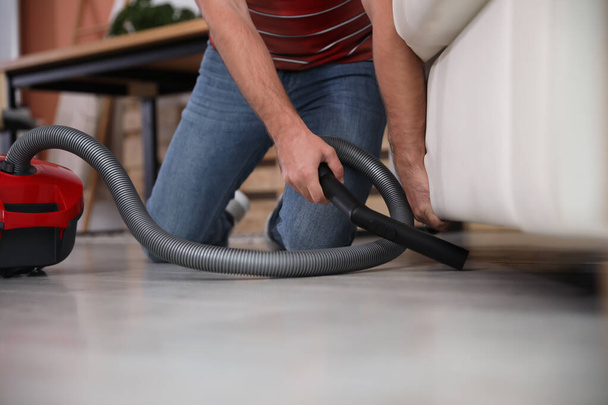 Young man using vacuum cleaner in living room, closeup - Foto, imagen
