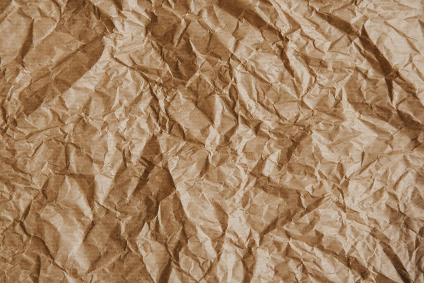 Wrinkled kraft brown paper as a background image. Coarse grain, crumpled, grunge texture detail. - Photo, Image