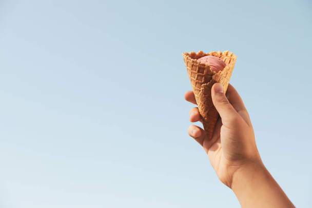 Woman holding delicious ice cream in waffle cone outdoors, closeup of hand. Space for text - Foto, Bild