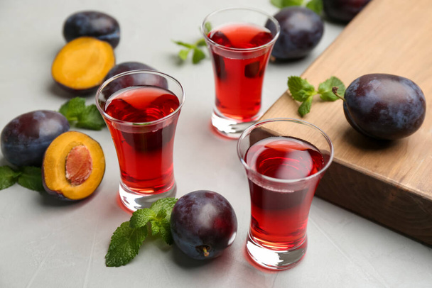 Delicious plum liquor, mint and ripe fruits on light table. Homemade strong alcoholic beverage - Foto, Imagen