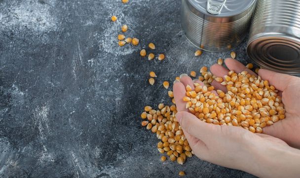 Χέρι κρατώντας ένα σωρό άψητα σπόρους ποπ κορν σε μαρμάρινο φόντο - Φωτογραφία, εικόνα