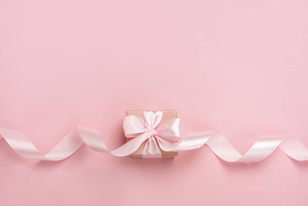 Gift box with long ribbon on pastel pink background. Present for Valentines Day, Mother's Day or Women's Day. Festive monochrome background. Top view flat lay with free space. - Фото, изображение
