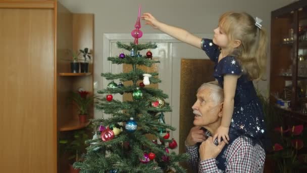 Kislány és idős nagyapa díszítő mesterséges karácsonyfa otthon, lassított felvétel - Felvétel, videó