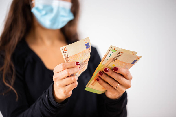 Jeune femme comptant l'argent et portant un masque chirurgical bleu - Photo, image