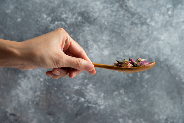 Hand holding a wooden spoon with dried roses - Foto, afbeelding