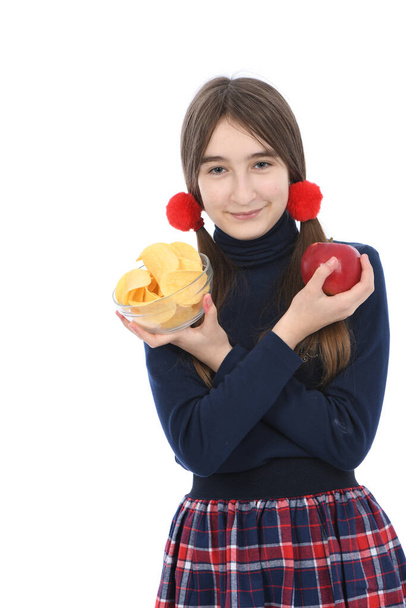 Teini-ikäinen tyttö painaa kulhot täynnä perunalastuja ja punaista omenaa. Eristetty valkoisella taustalla. Korkean resoluution kuva. Täysi syvyys. Käsitys terveellisen ja epäterveellisen ruoan valinnasta - Valokuva, kuva