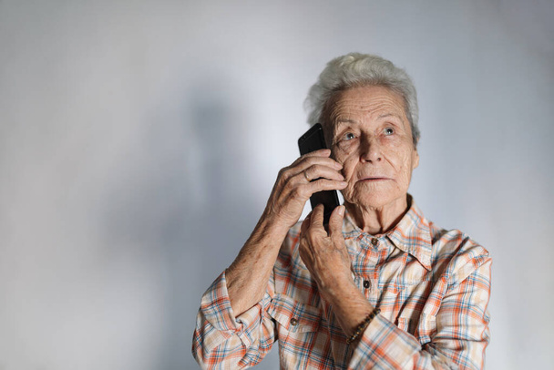 Ηλικιωμένη γυναίκα κάνει ένα τηλεφώνημα από το smartphone της. Τεχνολογική έννοια. - Φωτογραφία, εικόνα