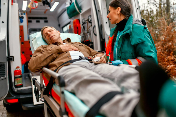 Sanitäter holen einen älteren Patienten aus einem modernen Krankenwagen zur weiteren medizinischen Versorgung in die Klinik. - Foto, Bild