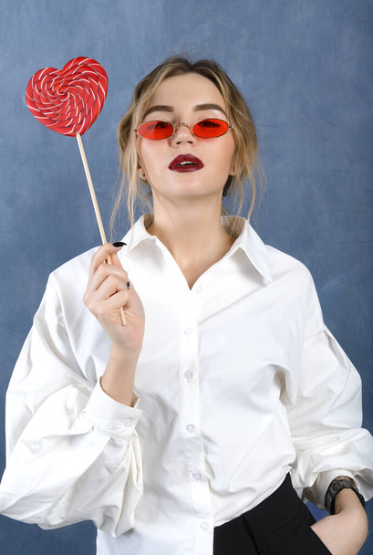1 біла блондинка в білій сорочці, в червоних окулярах з червоним серцем на сірому фоні
 - Фото, зображення