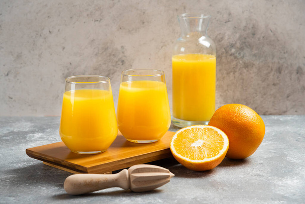 Glass cups of orange juice and a wooden reamer - Foto, afbeelding